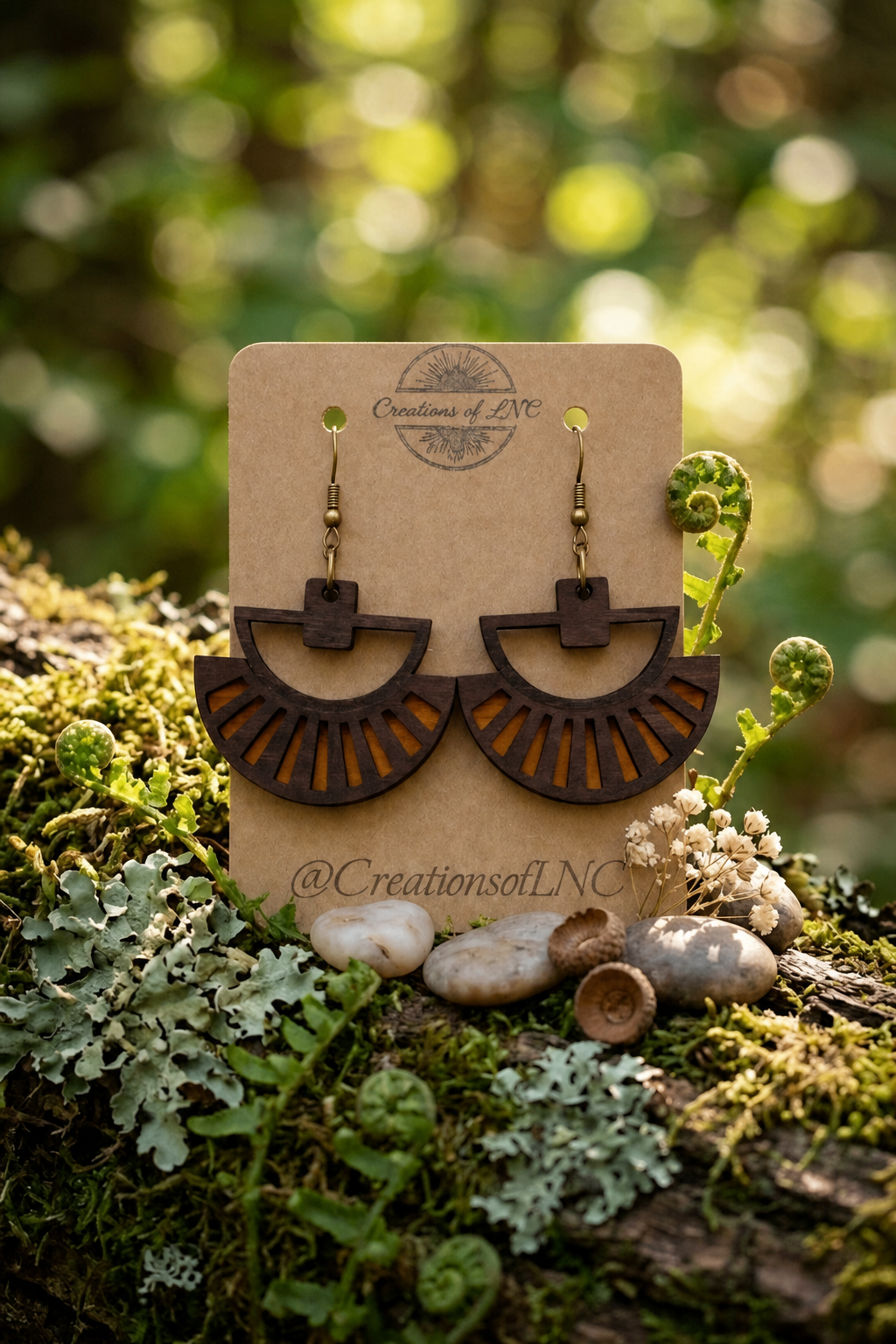 Dark wood fan earrings displayed among moss and ferns